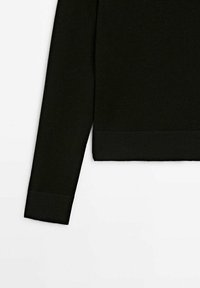Section d'un pull noir à manches longues montrant les poignets et la ceinture côtelés sur un fond blanc uni.