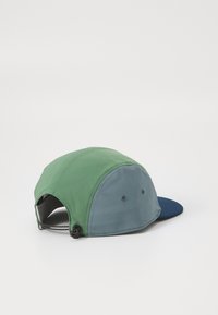 Boné verde e cinza com uma aba azul, feito de material macio. Apresenta um fecho de correr na parte de trás e dois buracos de ventilação nas laterais.