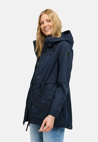 Marinblå vattentät parka med huva, dragkedja, tryckknappar, justerbart dragsnöre i midjan och sidofickor. Slät textur och ventilerande tyg.