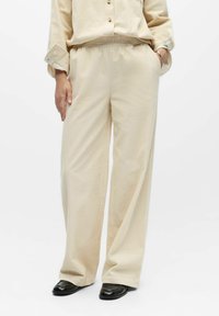 Pantalones beige de pierna ancha con superficie texturizada, cintura elástica, bolsillos laterales y ajuste holgado, combinados con una parte superior a juego.