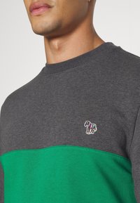 Sudadera bloqueada en gris y verde con cuello redondo; presenta un pequeño bordado de cebra multicolor en el pecho, fabricada en mezcla de algodón.