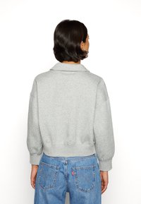 Grå kortärmad sweatshirt med krage, långa ärmar och ribbad fåll. Bärs med blå högmidjade jeans med bakfickor.