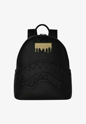 Zaino nero con motivo a denti di squalo in rilievo sul davanti e patch dorato con effetto goccia e scritta "Sprayground" in alto al centro.