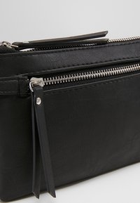 Musta nahkaranneke hopeisilla vetoketjuilla, teksturoidulla pinnalla ja kapealla, suorakaiteen muotoisella rakenteella. Varustettu koristeellisella vetoketjun vetimellä.