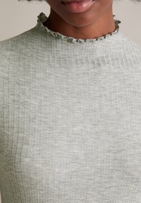 Hellgraues, geripptes Kurzarmoberteil mit hohem Kragen und fransigen Kanten, aus einem weichen, strukturierten Stoff.