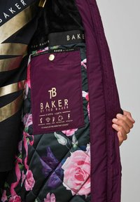 Doublure intérieure de la veste matelassée violette présentant une doublure florale, une étiquette de marque imprimée en or et des symboles d'entretien. Texture douce avec une finition résistante à l'eau.