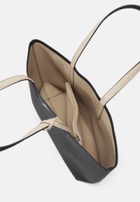 Sac fourre-tout en cuir noir avec intérieur beige, doté de deux poignées, d'une poche zippée et d'un tissu texturé pour une meilleure prise en main.