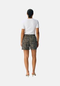 Camiseta blanca ajustada de manga corta combinada con pantalones cortos negros de longitud a la rodilla con un diseño de estampado de leopardo. Tela suave, ajuste casual.