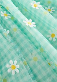 Tela de tul color aqua claro con un patrón de cuadros vichy y margaritas blancas bordadas con centros amarillos, creando una textura en capas.