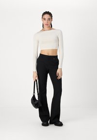 Haut cropped crème à manches longues associé à un pantalon noir évasé. Les accessoires incluent un petit sac noir et des chaussures noires épaisses.