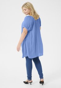 Tunic azzurro chiaro a maniche corte con tessuto testurizzato, vestibilità rilassata e pieghe sul retro, abbinata a jeans skinny blu scuro e tacchi neri.