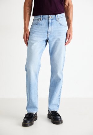 Man wearing light blue straight-leg jeans and black leather loafers, standing against a plain white background.