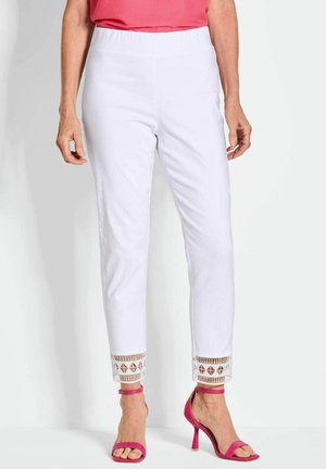 Pantalons blancs avec une taille élastique, ornés d'une garniture décorative aux poignets avec des motifs géométriques. Associés à des talons roses à lanières.