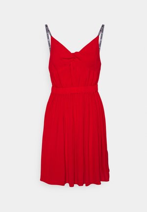 Robe rouge sans manches avec taille froncée, détail noué au niveau de la poitrine, et fines bretelles noires et blanches de la marque Tommy Jeans.