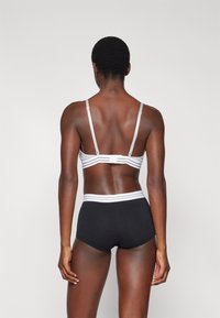 Bralette gris avec fines bretelles et fermeture à crochet, associé à une culotte taille haute noire avec une ceinture à rayures blanches.