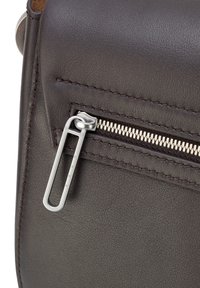 Coin d'un sac en cuir brun avec une fermeture éclair argentée, une surface texturée et des détails de couture contrastants. Le tirette de la fermeture est une boucle métallique.