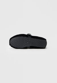 Sort sål af accessories med struktureret gummi for greb, med en rund form og blødt, fuzzy overmateriale. Accentueret med en simpel rem.