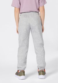 Pantalones de chándal grises con cintura elástica, que presentan una tela ligeramente texturizada y piernas ajustadas, combinados con zapatillas deportivas multicolores.