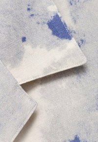 Stoff mit einem hellbeigen Grund, der mit einem Aquarellmuster in Blau verziert ist. Die Textur ist weich, mit sichtbaren Nähten an den Kanten.