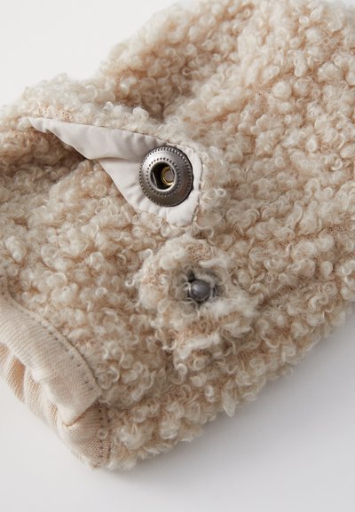 Μπεζ φουσκωτό ύφασμα τσάντα με υφή, με μεταλλικό κουμπί και υφασμάτινες λεπτομέρειες. Στρογγυλεμένες γωνίες, απαλό εμφάνιση.