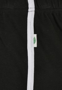 Black fabric shorts with white side stripe and green leaf logo tag. Soft texture, elastic waistband, casual design.