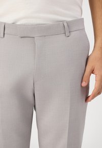 Light gray tailored trousers with a smooth texture, flat front, and belt loops. Features a subtle crease down the front and side hand pockets.