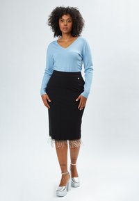 Maglione azzurro chiaro a scollo a V, gonna nera a tubino con orlo sfilacciato e scarpe con plateau argentate. La gonna presenta un accento decorativo in metallo.