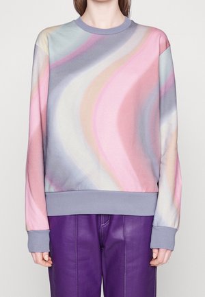 Personne portant un sweat-shirt à col rond à manches longues avec des motifs ondulés pastel rose, bleu, violet et beige, associé à un pantalon violet.
