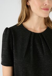 Abito nero a maniche corte, con un tessuto testurizzato e sottili luccichii, e morbide pieghe sul colletto.