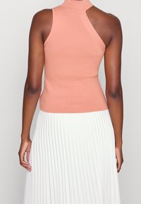 Top sin mangas ajustado en suave punto acanalado de melocotón, con un cuello alto y un corte en la parte posterior, combinado con una falda blanca plisada y fluida.