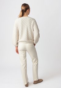 Kremasti džemper s reljefnim uzorkom dijamanta, uparen s svijetlosmešavim suknjama sužavajući se i smešnim braon cipelama. Pogled pozadi, kosa vezana u rep.