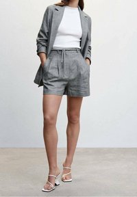 Blazer strutturato grigio chiaro con pantaloni corti abbinati realizzati in tessuto testurizzato. Top bianco aderente sotto e sandali con tacco bianchi open-toe.