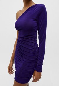 Lila, enaxlad klänning gjord av stretchmaterial; har rynkade detaljer längs kroppen för textur, med en kroppsnära silhuett.