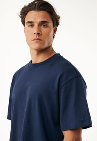 Camiseta de manga corta azul marino hecha de una tela suave, con un corte relajado, escote redondo y un sutil detalle del logo en la manga.