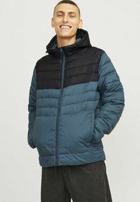 Chaqueta acolchada con un diseño bicolor en azul oscuro y negro, con cierre de cremallera y capucha. Textura suave con acentos de canalé.