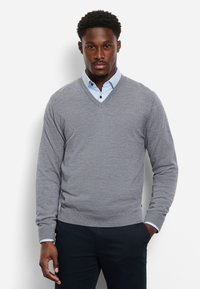 Maglione grigio lavorato a maglia con scollo a V, indossato sopra una camicia azzurro chiaro con colletto, abbinato a pantaloni blu navy scuro. Aspetto semplice e pulito.