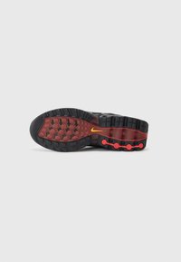 Nike sporta apavu zole melnā krāsā ar sarkaniem akcentiem; piedāvā teksturētu gumiju labākai saķerei, izteiksmīgus izciļņus un redzamu zīmola logo dzeltenā krāsā.