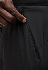 Χέρι που τραβάει το πλαϊνό τσέπη μαύρου παντελονιού, δείχνοντας το βάθος της τσέπης και την υφή του υφάσματος.