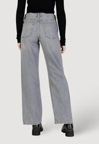 Jeans grigi ampi in denim con vita alta. Presentano due tasche posteriori e un orlo pulito. Indossati con stivaletti neri.