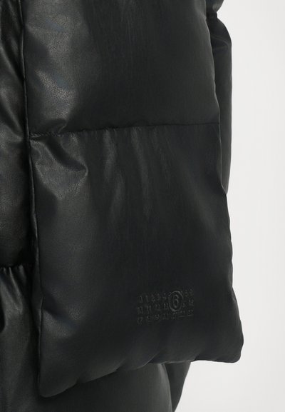 Μαύρο επενδυμένο μπουφάν με λείο εξωτερικό από συνθετικό δέρμα, ραφή τύπου καπιτονέ, μεγάλες ενότητες και διακριτό ανάγλυφο λογότυπο στην τσέπη.