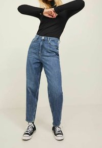 Hochtaillierte, mittelblaue Jeans aus Denim mit geradem Schnitt, fünf Taschen und umgeschlagenen Säumen, kombiniert mit schwarzen Turnschuhen.