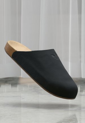 Black slip-on clog made of textured leather with a cork sole. Features a smooth, rounded shape and a subtle logo detail on the side.