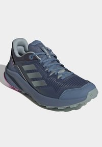Zapatilla deportiva azul con parte superior de malla, detalles en gris y suela con patrón. Marca notable en el costado y cuello acolchado.