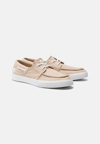 Beige Canvas-Schuhe mit weißen Gummisohlen, Schnürdesign, genähten Akzenten und Logodetail an der Seite. Glatte Oberfläche.