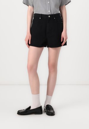 Black denim shorts with a straight cut, front pockets, and a frayed hem, paired with black loafers and light gray socks.