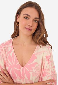 Blusa a fiori color crema con disegni rosa. Scollo a V, maniche corte e dettagli texturizzati. Tessuto morbido e leggero.