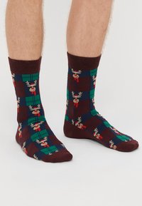 Sötétbarna zoknik rénszarvasok és zöld, kék, valamint piros négyzetek mintájával. Kötött anyagból készült, bordás szárakkal.