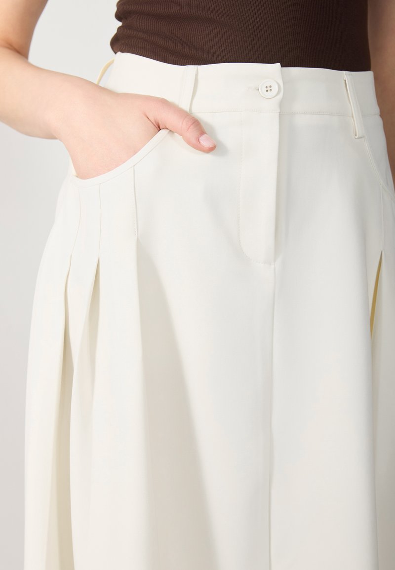 Weiße, gefaltete Hosen mit flachem Front, seitlichen Taschen und einem einzigen Knopfverschluss an der Taille. Glatte Stoffoberfläche.