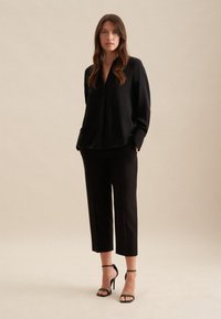 Czarna, długosleeve bluzka z dekoltem w serek, zestawiona z dopasowanymi czarnymi spodniami 3/4 i czarnymi sandałami na wysokim obcasie. Gładka tekstura materiału.