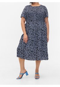 Czarna sukienka w kwiaty z krótkimi rękawami, z małymi niebieskimi kwiatami, zebranym pasem i długości midi. Noszona z niebieskimi sandałami na słupku.